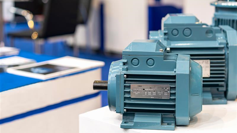 Close‑up of industrial electric motors displayed on a white table, with a focus on a blue motor featuring a metal nameplate and visible cooling fins